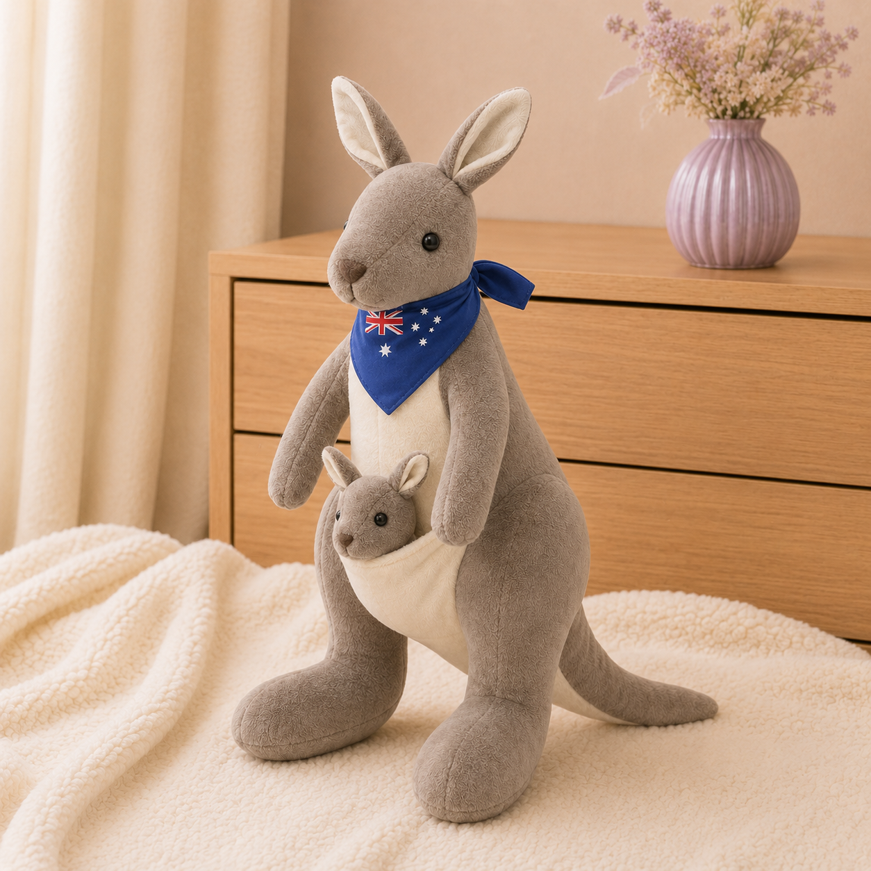 Peluche kangourou gris foncé avec son bébé posée sur une couverture ivoire près d'une commode
