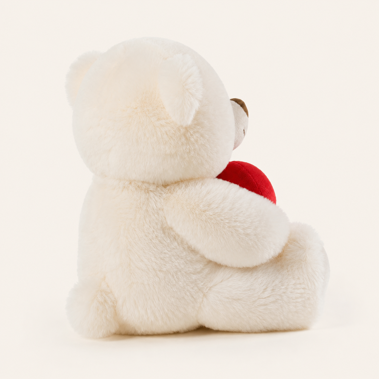 Peluche ourson blanche tenant un cœur rouge, vue arrière trois-quarts sur fond ivoire