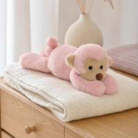 Peluche singe rose posée sur une couverture ivoire sur une commode en bois clair