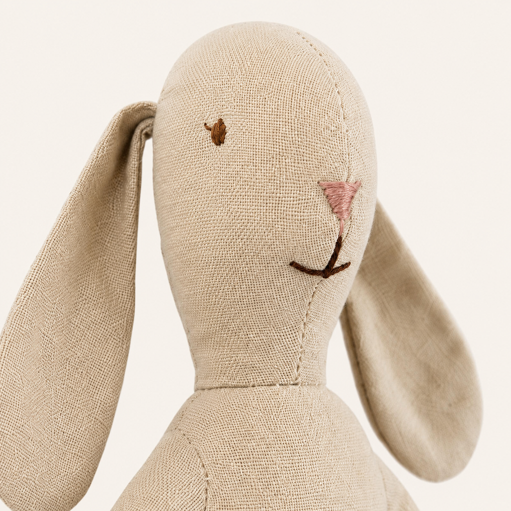Gros plan sur le visage brodé et le tissu beige du doudou lapin