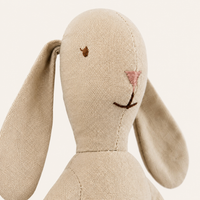 Gros plan sur le visage brodé et le tissu beige du doudou lapin