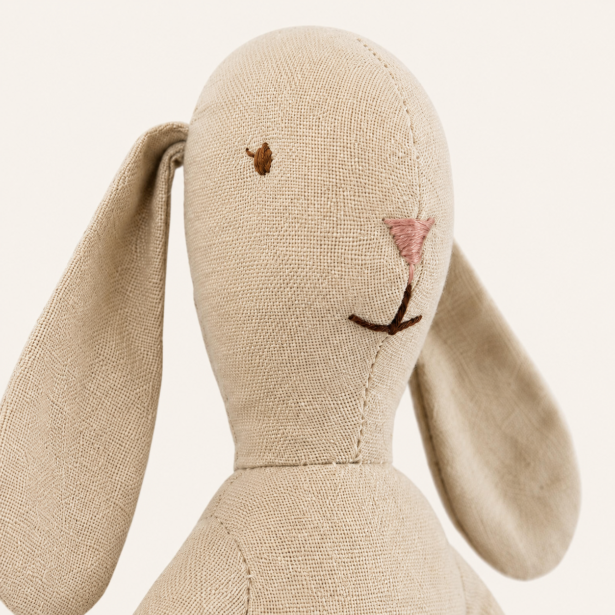 Gros plan sur le visage brodé et le tissu beige du doudou lapin