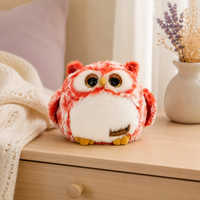 Peluche hibou rouge posée sur une commode en bois clair dans une chambre douce