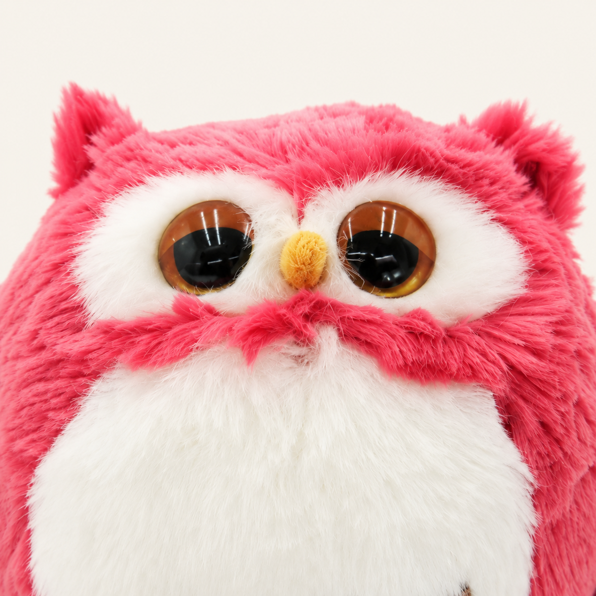 Gros plan sur les yeux, le bec et la fourrure de la peluche hibou rose