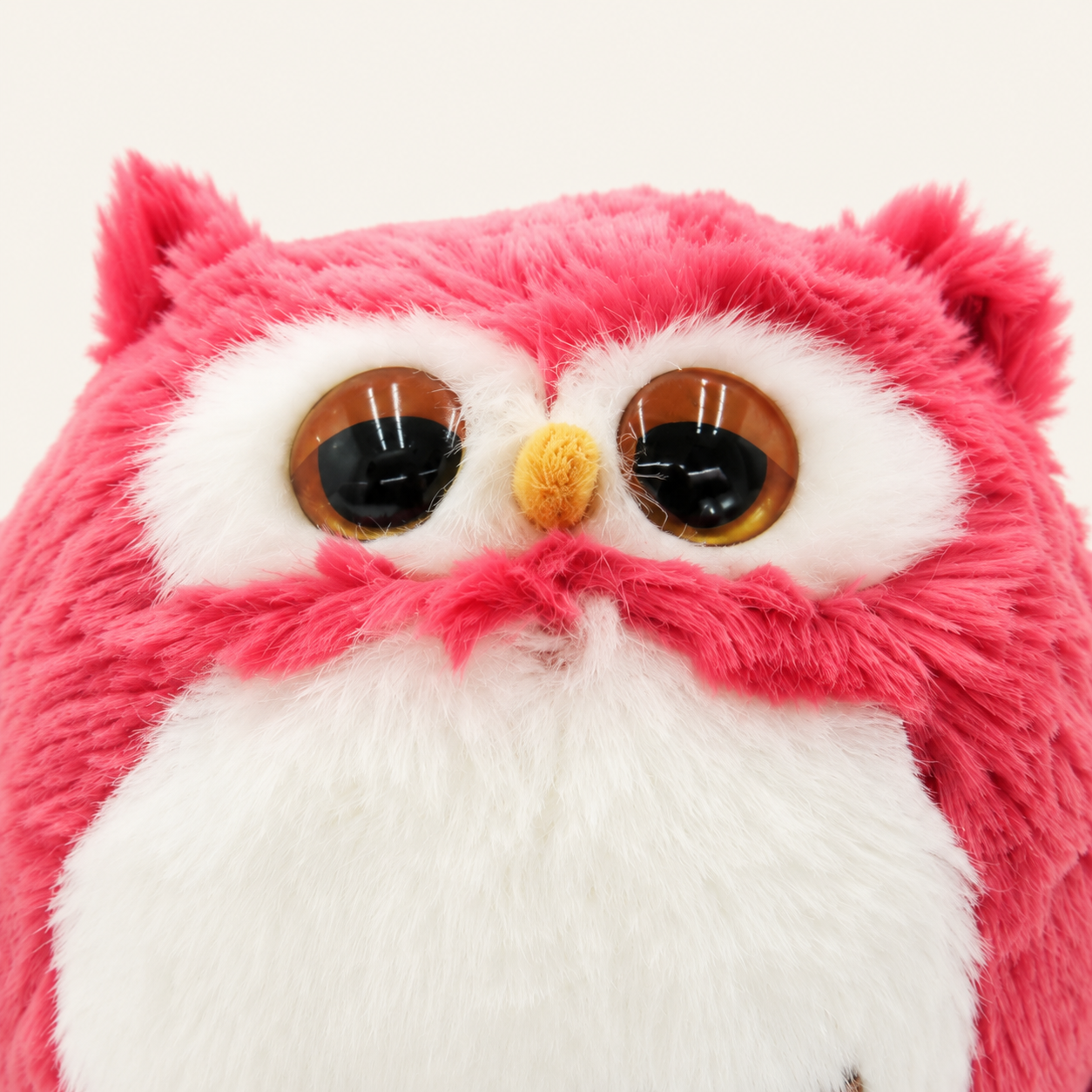 Gros plan sur les yeux, le bec et la fourrure de la peluche hibou rose