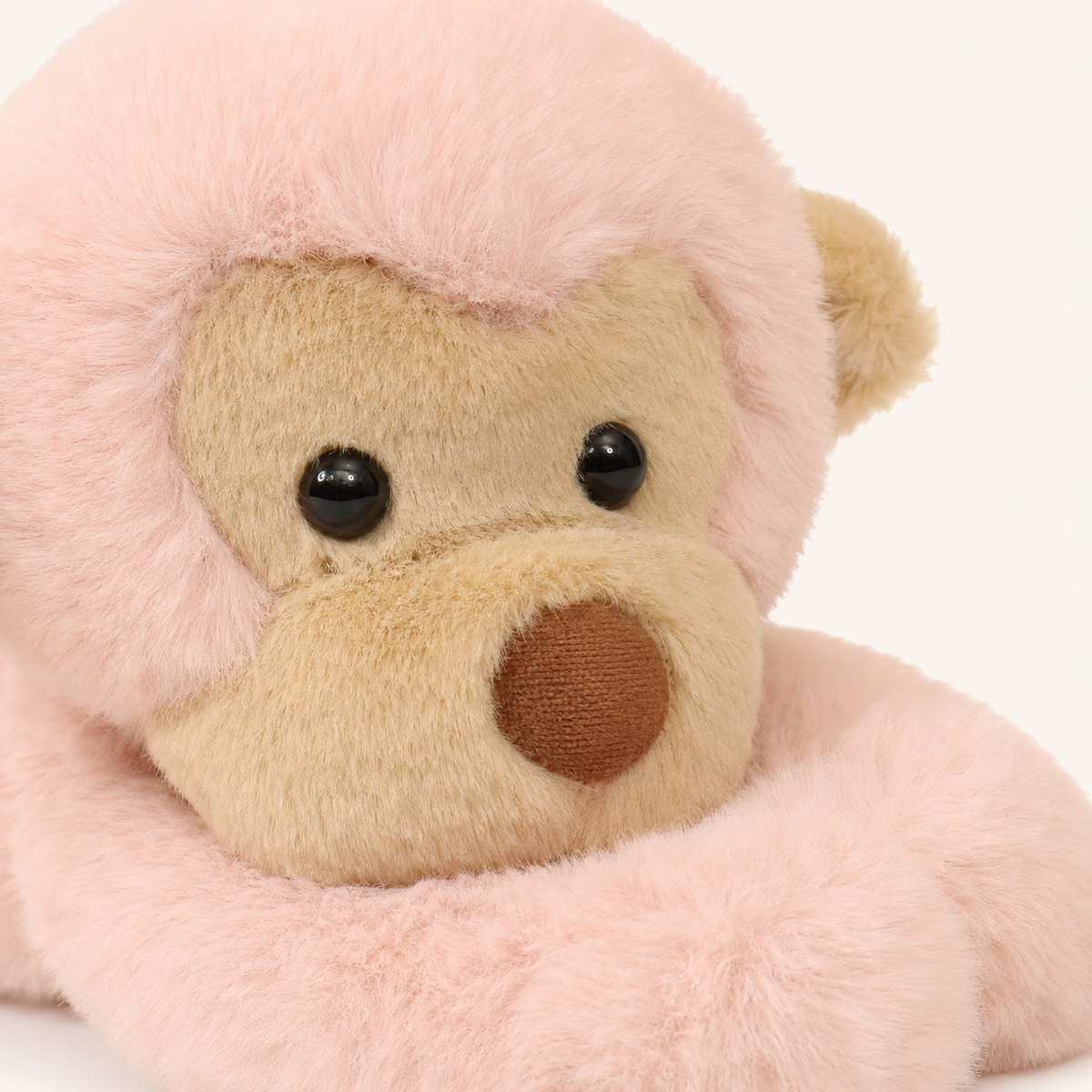 Gros plan sur le visage beige et la fourrure rose de la peluche singe