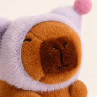 Gros plan visage peluche capybara au bonnet violet, fond ivoire