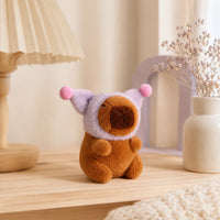 Peluche capybara au bonnet violet posee sur une etagere, mise en situation