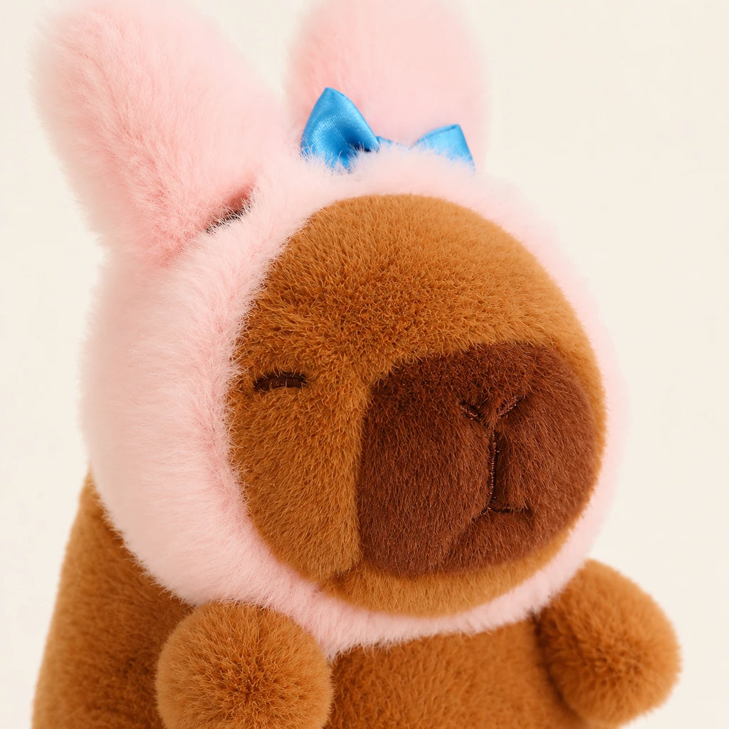 Gros plan visage peluche capybara bonnet lapin, fond ivoire