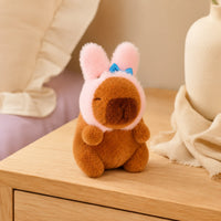 Peluche capybara bonnet lapin posee sur une commode, mise en situation