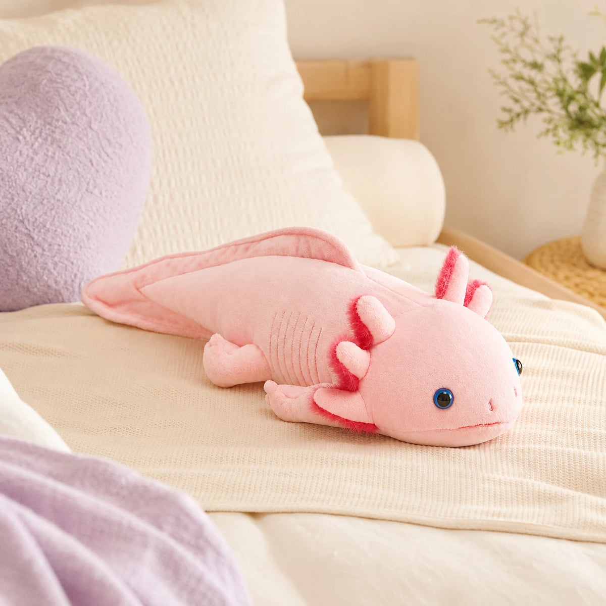 Peluche axolotl rose posée sur un lit douillet, mise en situation