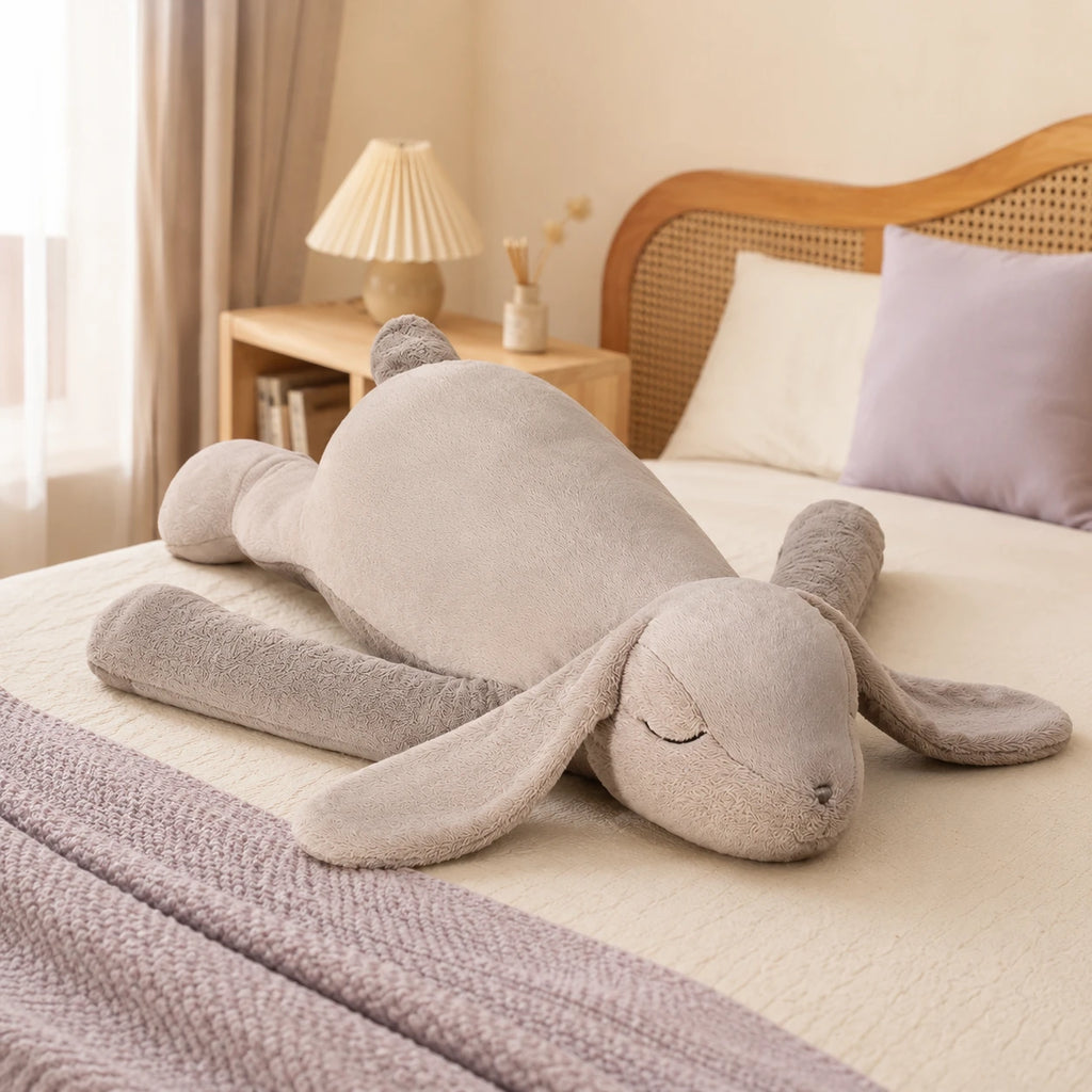 Grande peluche lapin gris couchée sur un lit, mise en situation cosy