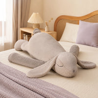 Grande peluche lapin gris couchée sur un lit, mise en situation cosy