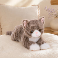 Peluche chat realiste gris posee sur un lit, mise en situation cosy