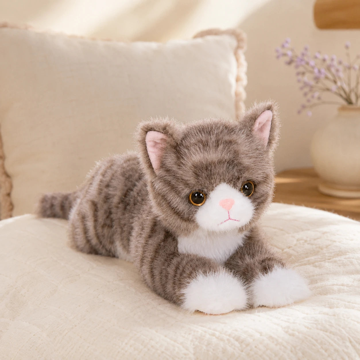Peluche chat realiste gris posee sur un lit, mise en situation cosy