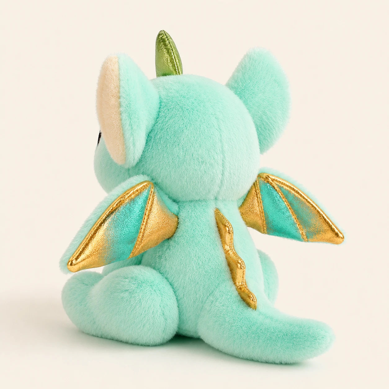 Peluche dragon vue de trois-quarts arrière montrant les ailes dorées
