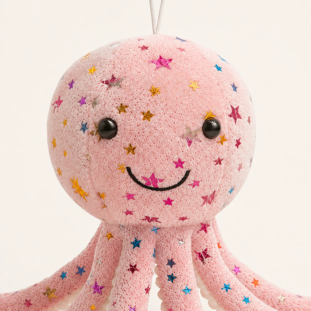Gros plan sur le visage souriant et les étoiles brodées de la peluche pieuvre rose