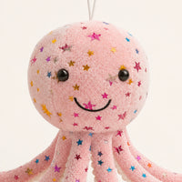 Gros plan sur le visage souriant et les étoiles brodées de la peluche pieuvre rose