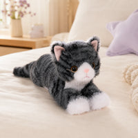 Peluche chat gris tigré posée sur un lit cosy