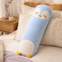 Coussin long peluche pingouin pose sur un lit douillet