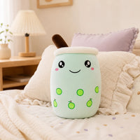 Peluche bubble tea vert pomme posee sur un lit douillet, ambiance chaleureuse