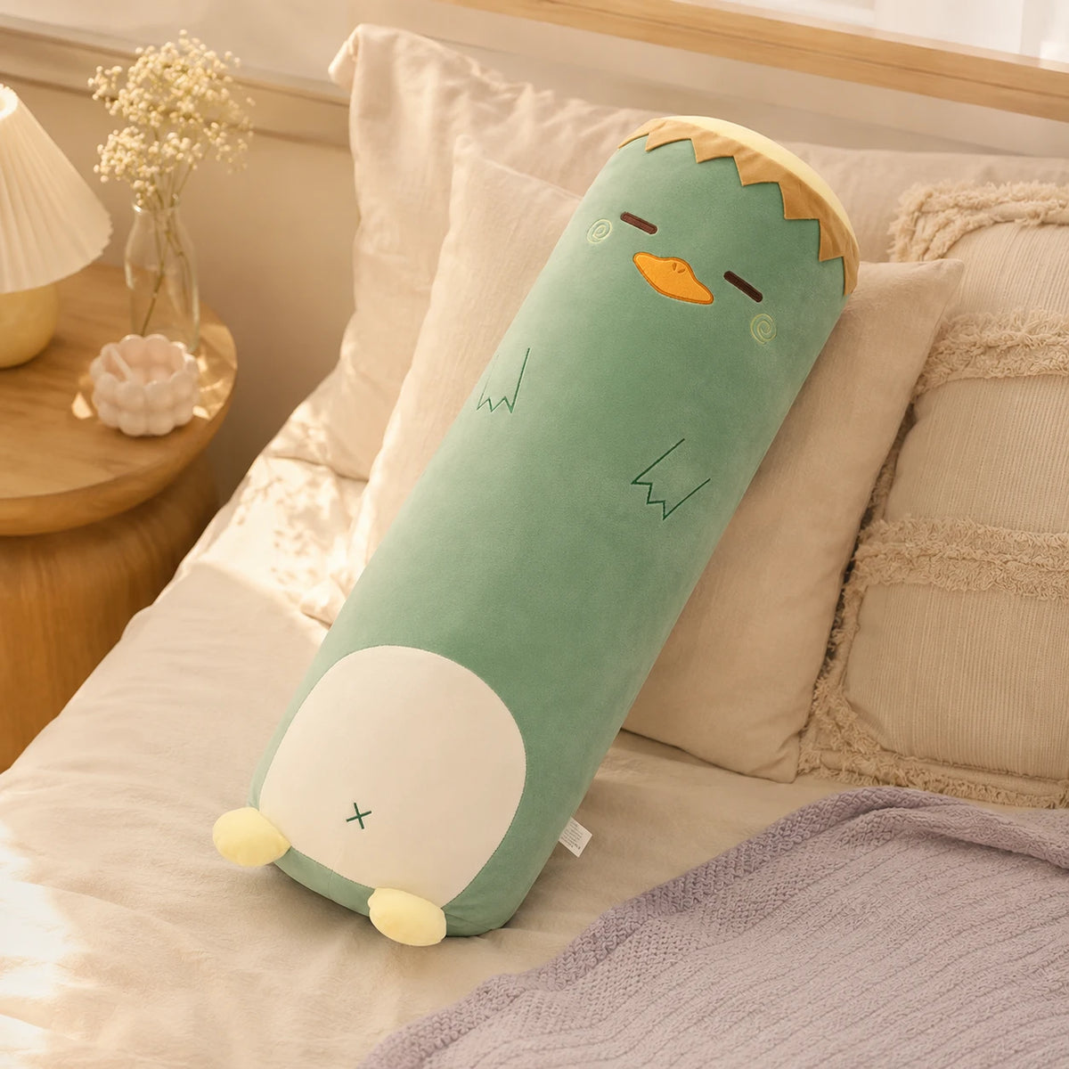 Coussin long peluche dinosaure pose sur un lit douillet