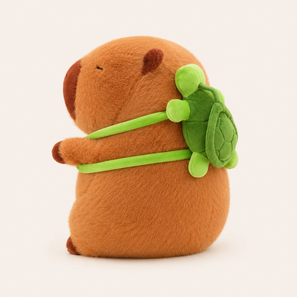 Peluche capybara, vue de trois-quarts montrant le sac à dos tortue, fond ivoire