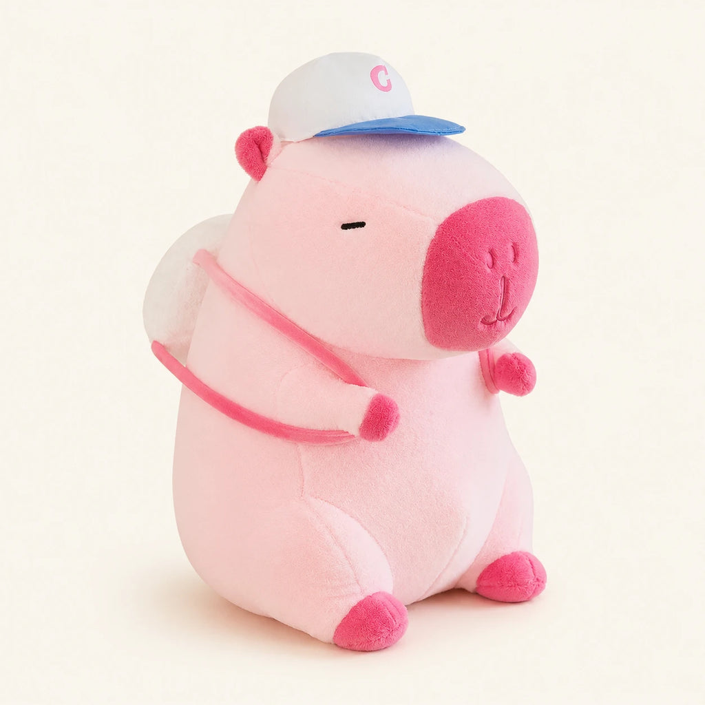 Peluche capybara rose avec casquette et sacoche, vue principale sur fond ivoire