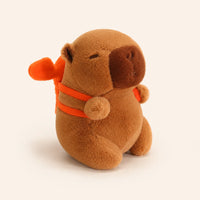 Peluche capybara brun avec petit sac à dos orange, vue de face sur fond ivoire