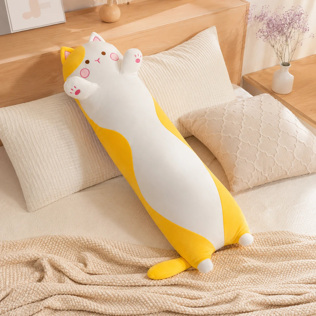 Coussin long peluche chat jaune pose sur un lit douillet