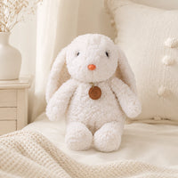 Peluche lapin blanc longues pattes 35 cm posée sur un lit