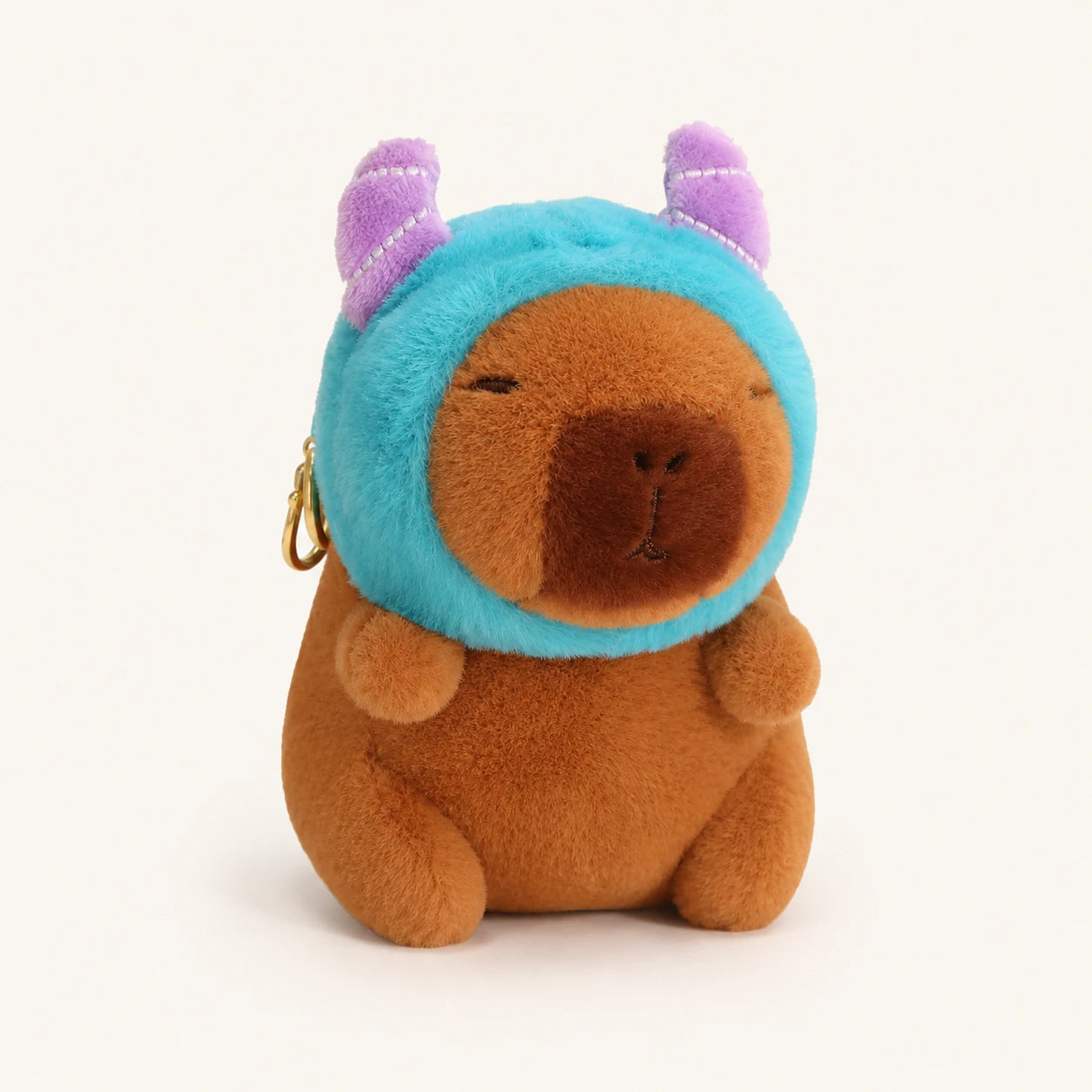 Peluche capybara brun coiffée d un bonnet bleu à cornes, vue de face sur fond ivoire