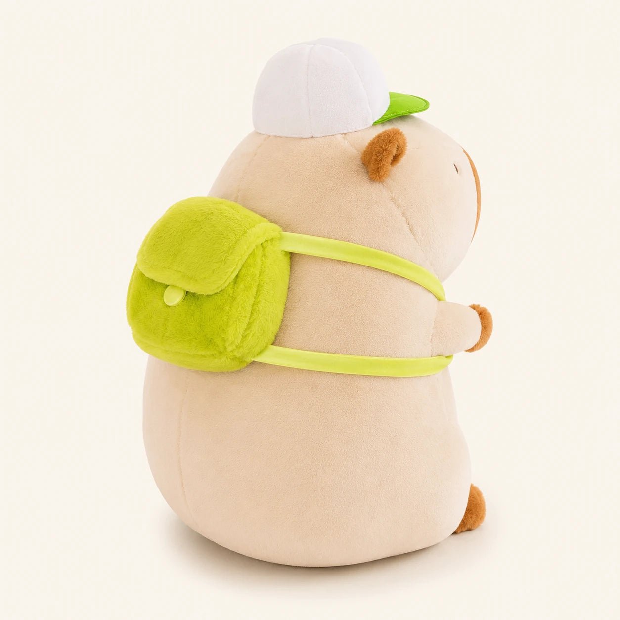 Peluche capybara creme, vue de trois-quarts arriere montrant le sac a dos vert
