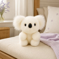 Peluche koala blanche posée sur un lit douillet, ambiance chaleureuse