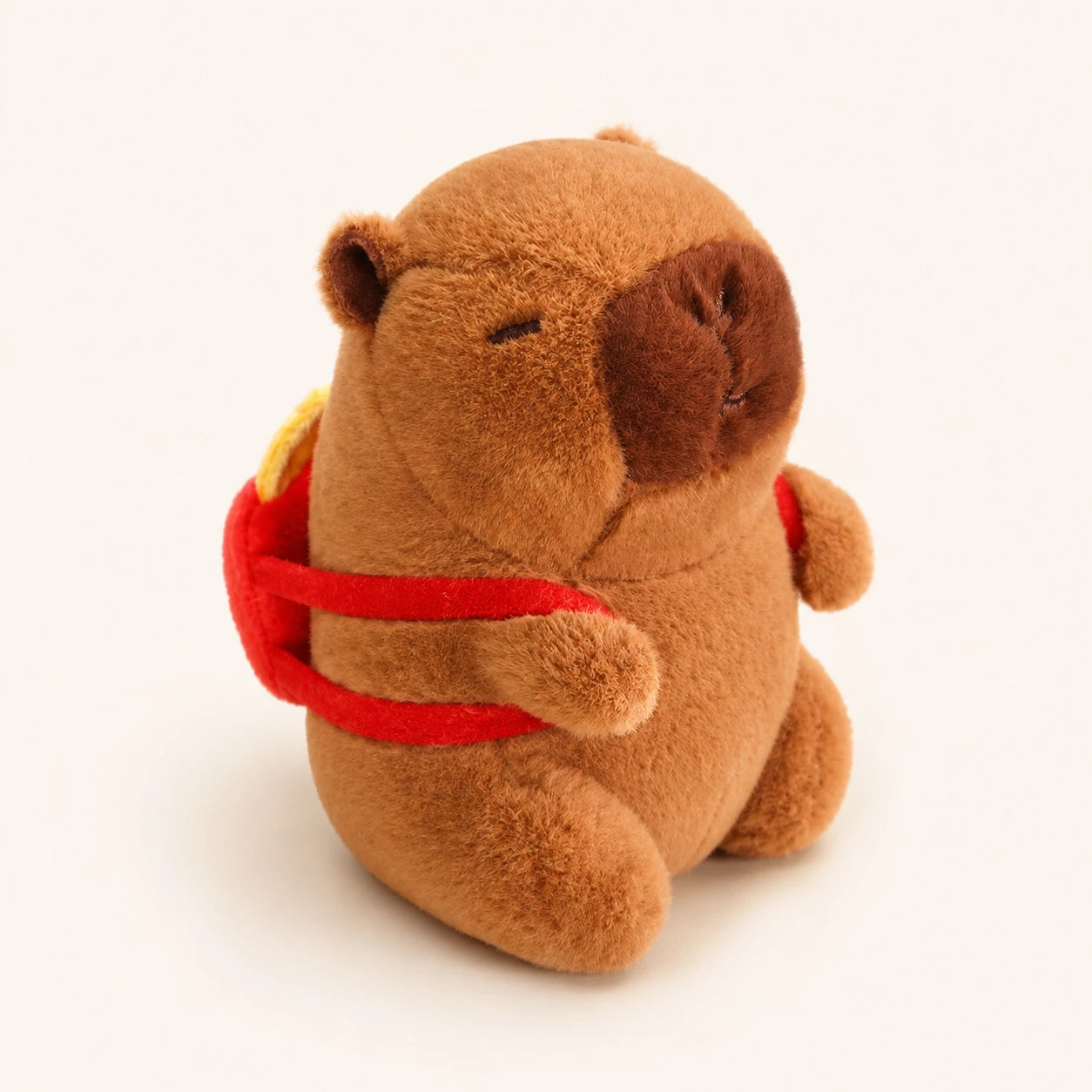Peluche capybara avec sac à dos rouge, vue de face, fond ivoire
