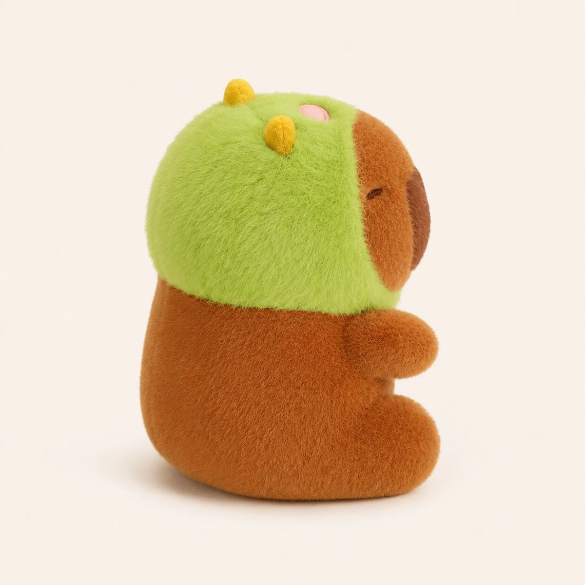 Peluche capybara vue de trois-quarts, capuche verte, fond ivoire